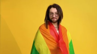 Genç aktivist gülümseyen neşeli gay adam sarı arka plan stüdyosunda izole edilmiş gökkuşağı bayrağı sallıyor. İnsanlar yaşam tarzı kavramını seviyorlar.