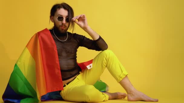 年轻的高加索基佬20多岁 带着彩虹条纹旗坐在黄色的背景上 人们的生活方式时尚Lgbtq概念 — 图库视频影像