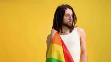 Genç aktivist gülümseyen neşeli gay adam sarı arka plan stüdyosunda izole edilmiş gökkuşağı bayrağı sallıyor. İnsanlar yaşam tarzı kavramını seviyorlar.