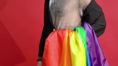 Kırmızı arka planda örgü tişört ve güneş gözlüğü takmış renkli gökkuşağı bayrağı olan eşcinsel bir adam. Farklılık, transseksüel ve özgürlük kavramları