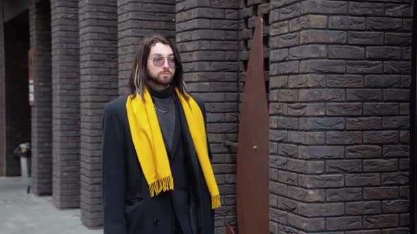 若い白人スタイリッシュな男が黄色のスカーフでコートを着て通りを歩く — ストック動画