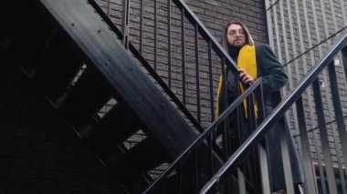 Sarı çantayla alışveriş yaptıktan sonra paltosu ve sarı atkısı olan beyaz bir adam..