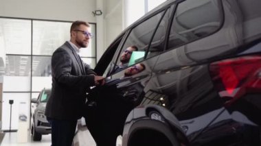 Bir adam araba galerisinde yeni arabanın kapısını kapatır. Satın almadan önce aracı inceleyen bir adam. Araba al.