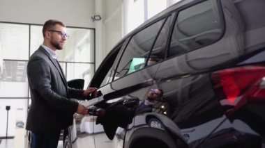 Bir adam araba galerisinde yeni arabanın kapısını kapatır. Satın almadan önce aracı inceleyen bir adam. Araba al.