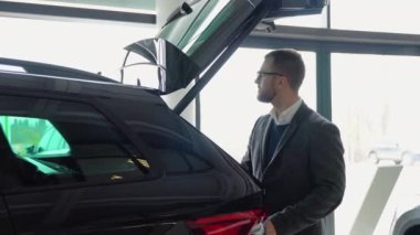 Bir adam araba galerisinde yeni bir arabanın bagajını kapatıyor.