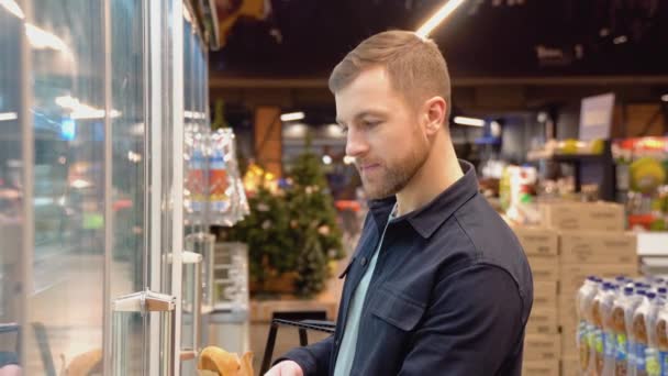 スーパーの乳業コーナーでの若い男の買い物 鶏の卵を買いながら市場で買い物をする男 — ストック動画