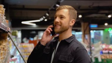 Süpermarkette alışveriş yapan kafası karışmış orta yaşlı bir adamın portresi: karısını arayıp hangi sağlıklı fındık ve kurutulmuş meyveyi seçeceğimi soruyor.