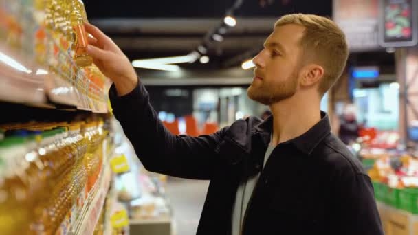 若い男がスーパーでオリーブを選ぶ スーパーの棚から食べ物を選ぶ — ストック動画