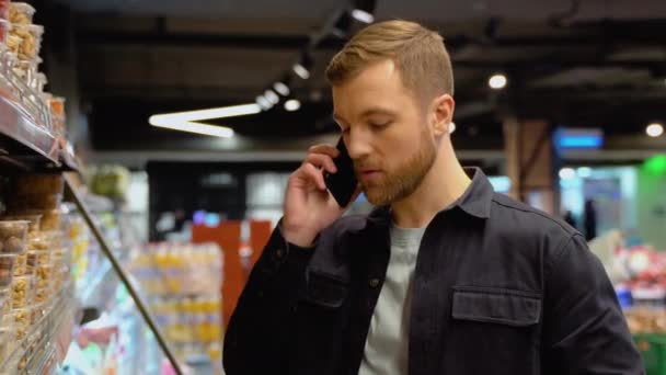Fiatal Kaukázusi Férfi Egy Szupermarketben Vásárol Termékeket Választ Telefonon Beszél — Stock videók