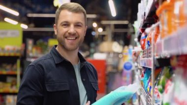 Genç, neşeli, pozitif erkek müşteri süpermarketten alışveriş yapıyor, ev yapımı kimyasallar alıyor..