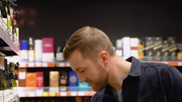 男はスーパーマーケットの棚から酒を飲む 店内でお酒を買う — ストック動画