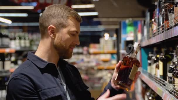 男はスーパーマーケットの棚から酒を飲む 店内でお酒を買う — ストック動画