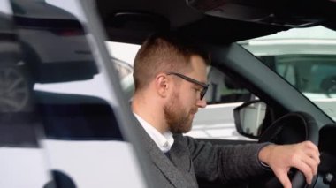 Bir araba galerisinde yeni bir lüks elektrikli araba kullanan mutlu ve şık bir adamın portresi. Alıcı bir araba seçer.