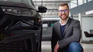 Araba galerisinde yeni bir arabanın yanında genç bir adamın portresi.