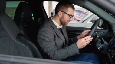 Mutlu adam atölyedeki yeni arabasında oturuyor ve yeni araba alımını kutluyor. Araba al.