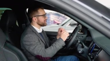 Mutlu adam atölyedeki yeni arabasında oturuyor ve yeni araba alımını kutluyor. Araba al..