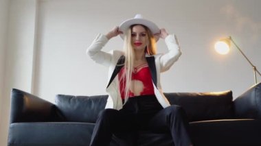 Boyalı saçlı, şapkalı, makyajlı beyaz ceketli ve kırmızı sutyenli bir kadın stüdyoda poz veriyor. Moda çekim konsepti.