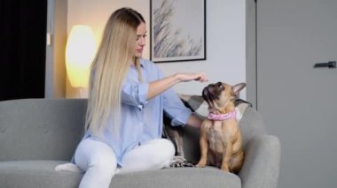 Güzel, sevimli, sıradan bir kadın, mutlu bir şekilde oyun oynayıp, takılıyor ve evin oturma odasındaki gri kanepede sevimli Fransız buldoguna sarılıyor.
