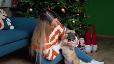 Hoş süveter giymiş şık bir kadın, süslü bir odada sevimli Fransız bulldog 'una sarılıyor..