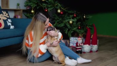 Hoş süveter giymiş şık bir kadın, süslü bir odada sevimli Fransız bulldog 'una sarılıyor..