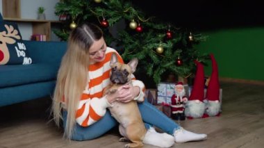 Hoş süveter giymiş şık bir kadın, süslü bir odada sevimli Fransız bulldog 'una sarılıyor..