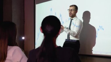 Digital enterpreneur presents cryptocurrency investment strategy for group of investors. Wall TV showing big data analysis, infographics, stock market information, trends