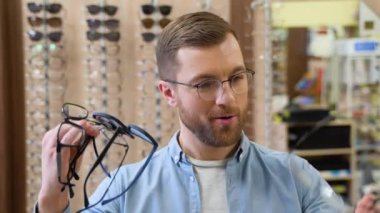 Excited surprised man holds many new glasses in his hands at optical shop. Choosing glasses concept.