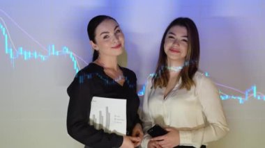 Two confident professional business woman in the office against the background of financial chart.