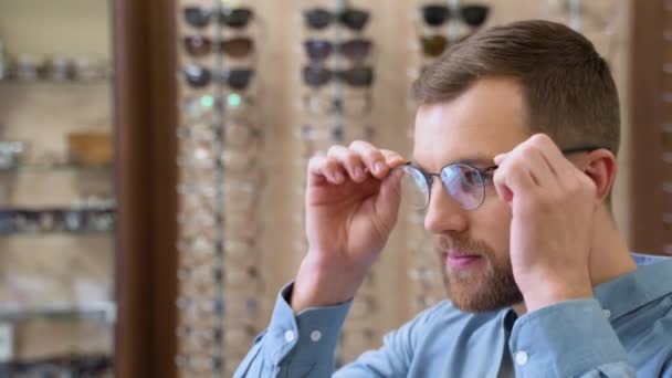 选择眼镜的概念 照片上英俊的大胡子男人在光学商店选新的镜片 看着镜子 — 图库视频影像