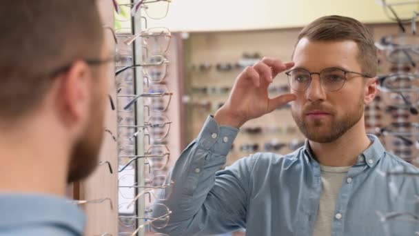 鏡を見て 光学店で新しい仕様を選ぶハンサムな髭の男の肖像画 メガネのコンセプトを選ぶ — ストック動画