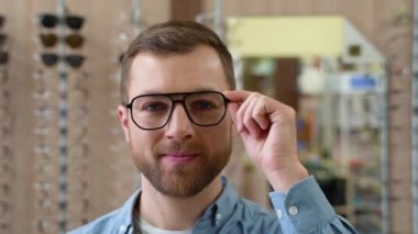 Portrait of handsome bearded guy picking new specs at optical shop, looking at camera. Choosing Glasses Concept.
