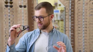 Health care, eyesight and vision concept - happy man choosing glasses at optics store.