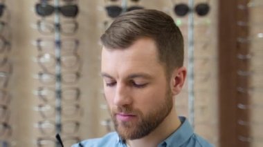 A funny man puts glasses incorrectly. A man is having fun in optics when choosing glasses.