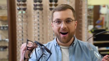 Excited surprised man holds many new glasses in his hands at optical shop. Choosing glasses concept.