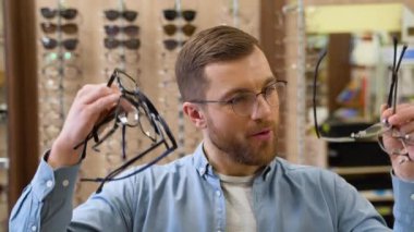 Excited surprised man holds many new glasses in his hands at optical shop. Choosing glasses concept.
