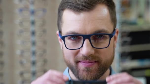 ポートレートのハンサムなひげを生やした男ピッキング新しいサングラスで光学店 — ストック動画
