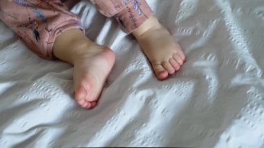 Sevimli masum bebek ilk bebek emeklediğinde yatakta emeklemeye çalışıyor. Güzel bebek kız pembe bebek elbisesi giyiyor. Küçük çocuk bacağını ve vücudunu kaldırmak için kullanmaya çalışıyor. Bacaklarını kapat..