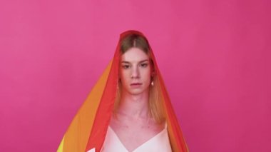 Beutiful young transgender man lifing rainbow flag from her head in the air.