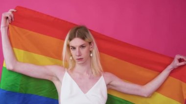 Gender fluid gay man with pride lgbt flag against pink background.