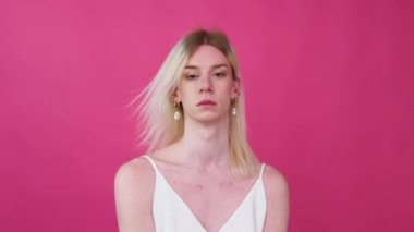 Portrait close up of young transgender man in a dress on a pink background