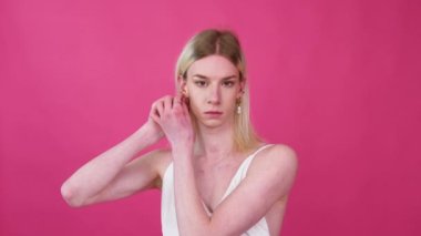 Portrait of young transgender man in a dress on a pink background
