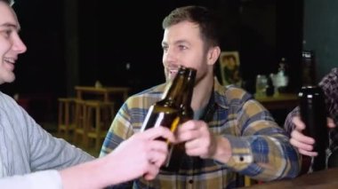 Group of happy young men drinking cold draft beer, chatting and having good time at pub. Smiling carefree friends enjoying drinking together in bar.