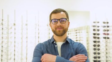 Happy young male client puts new glasses near rack and showcase with eyewear. Satisfied Customer.