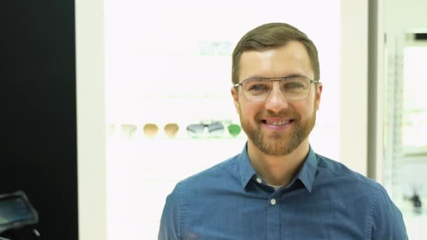 Happy Young Male Client Puts New Glasses Rack Showcase Eyewear — Vídeo de stock