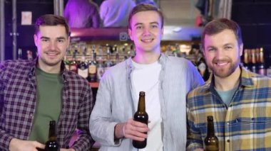 Group of happy young men drinking cold draft beer, chatting and having good time at pub. Smiling carefree friends enjoying drinking together in bar