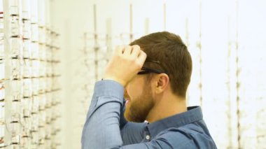 Portrait of a funny male client in several glasses near showcase with eyewear.