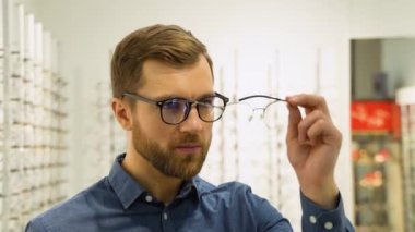 Health care, eyesight and vision concept - happy man choosing glasses at optics store