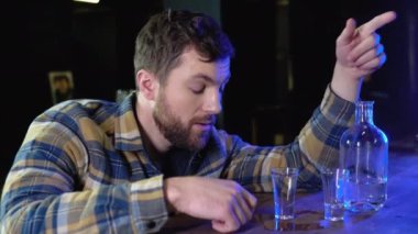 A very drunk young man is lying with his head on a table in a bar.