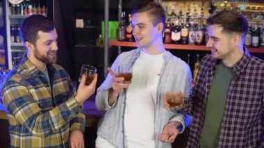 Three friends in a bar chatting and pouring whiskey from glasses.