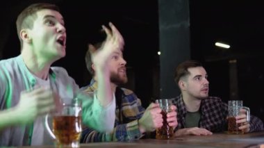 Group of friends watches TV in the sporstbar. Their team scores the goal and wins. Young people cheer.